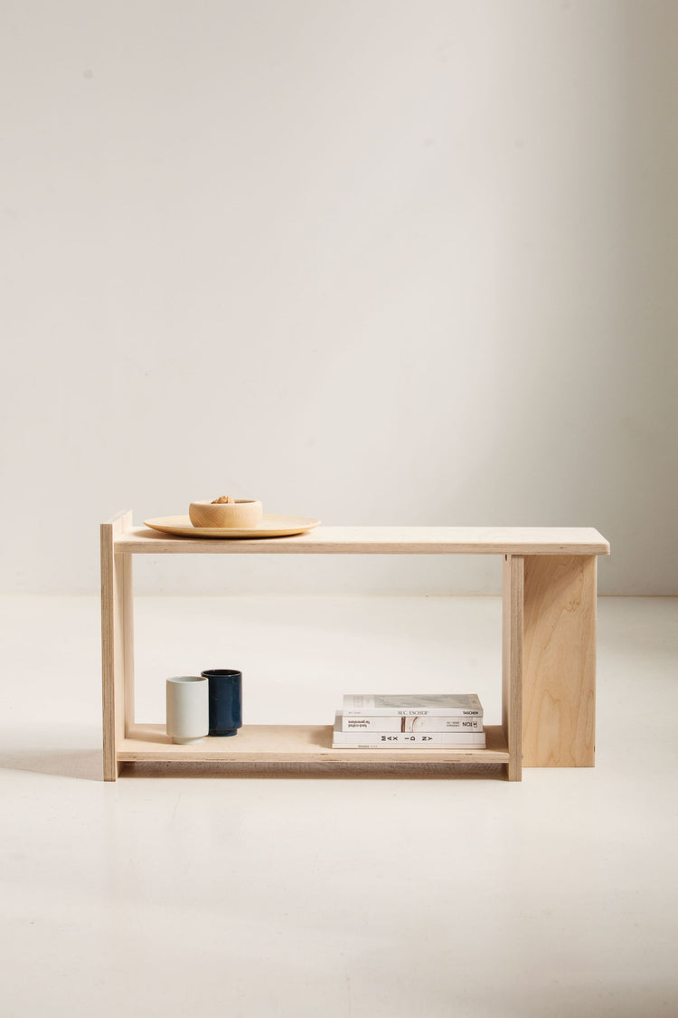 Minimalist wooden bench with a shelf against a plain wall.