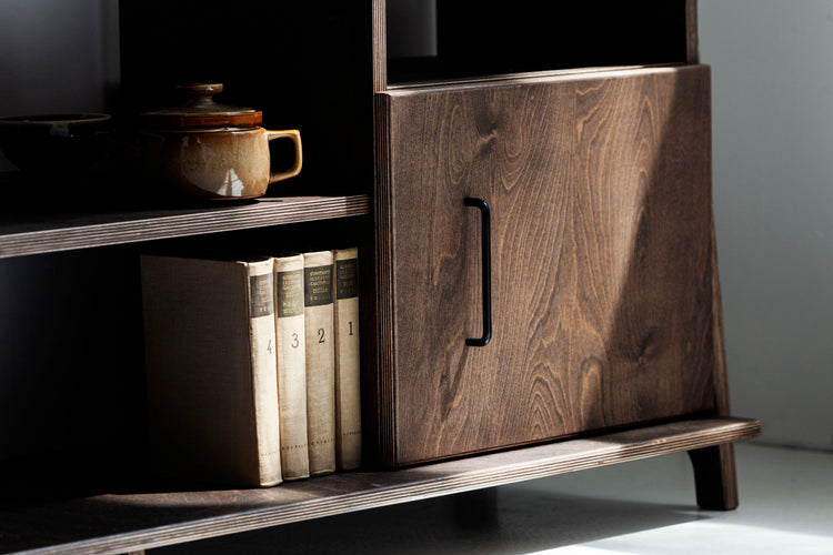 Wooden cabinet with books and a teapot on a shelf against a gray wall.