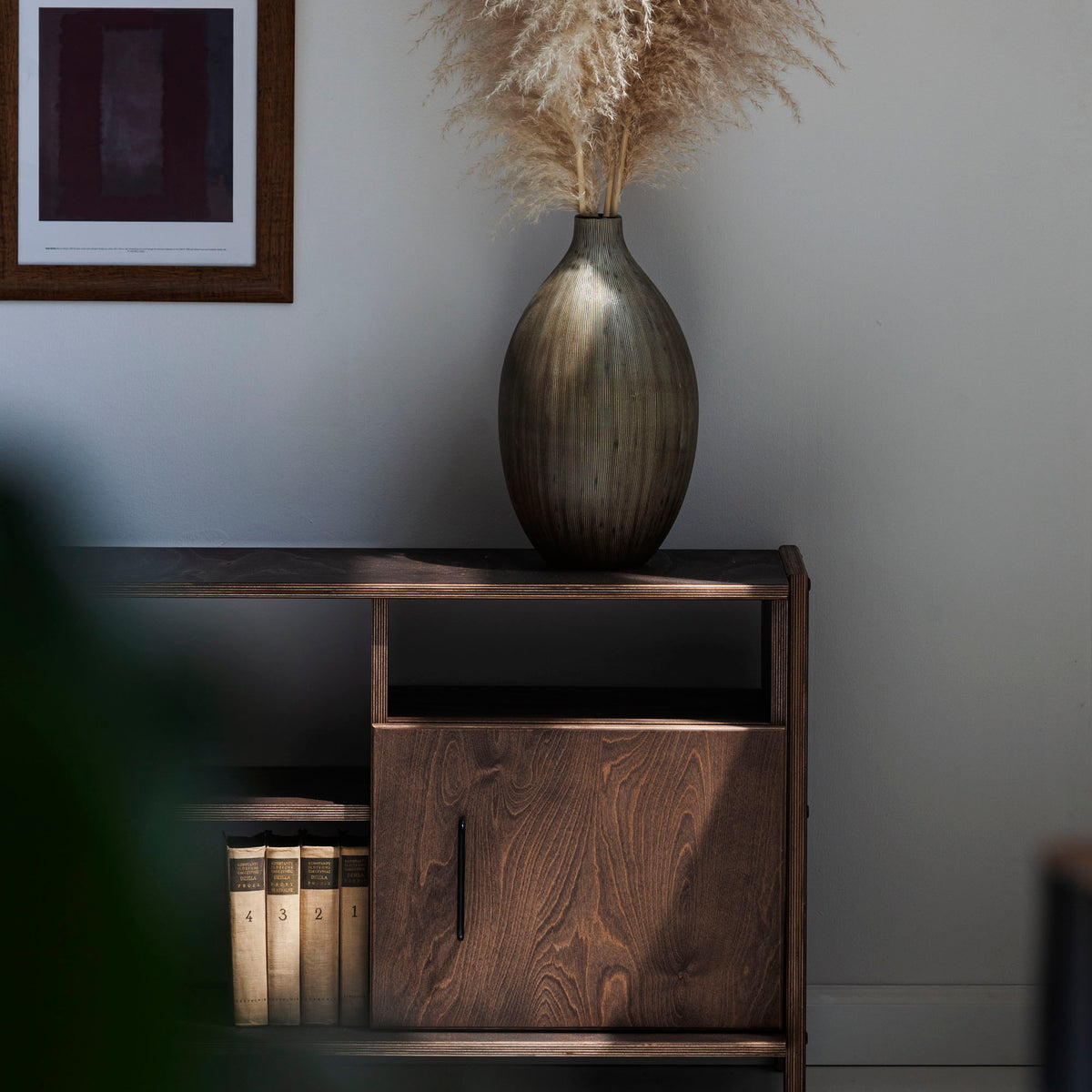 Wooden cabinet with a vase and pampas grass against a gray wall