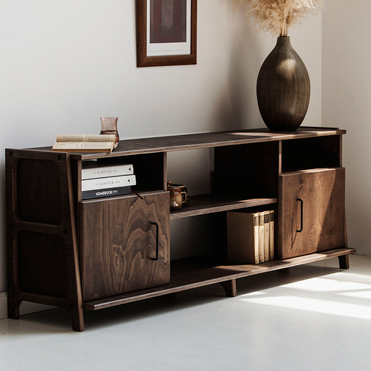 Wooden sideboard with decorative items in a room with a plant and framed picture.